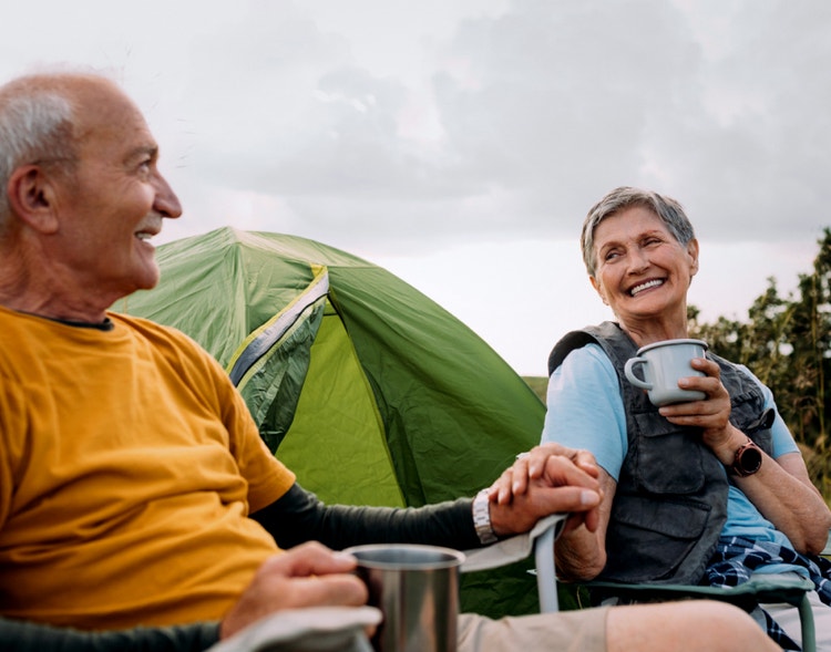 An elderly couple holding hands while camping