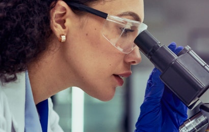 A woman in a lab coat looking into a microscope