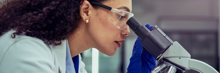 A woman in a lab coat looking into a microscope